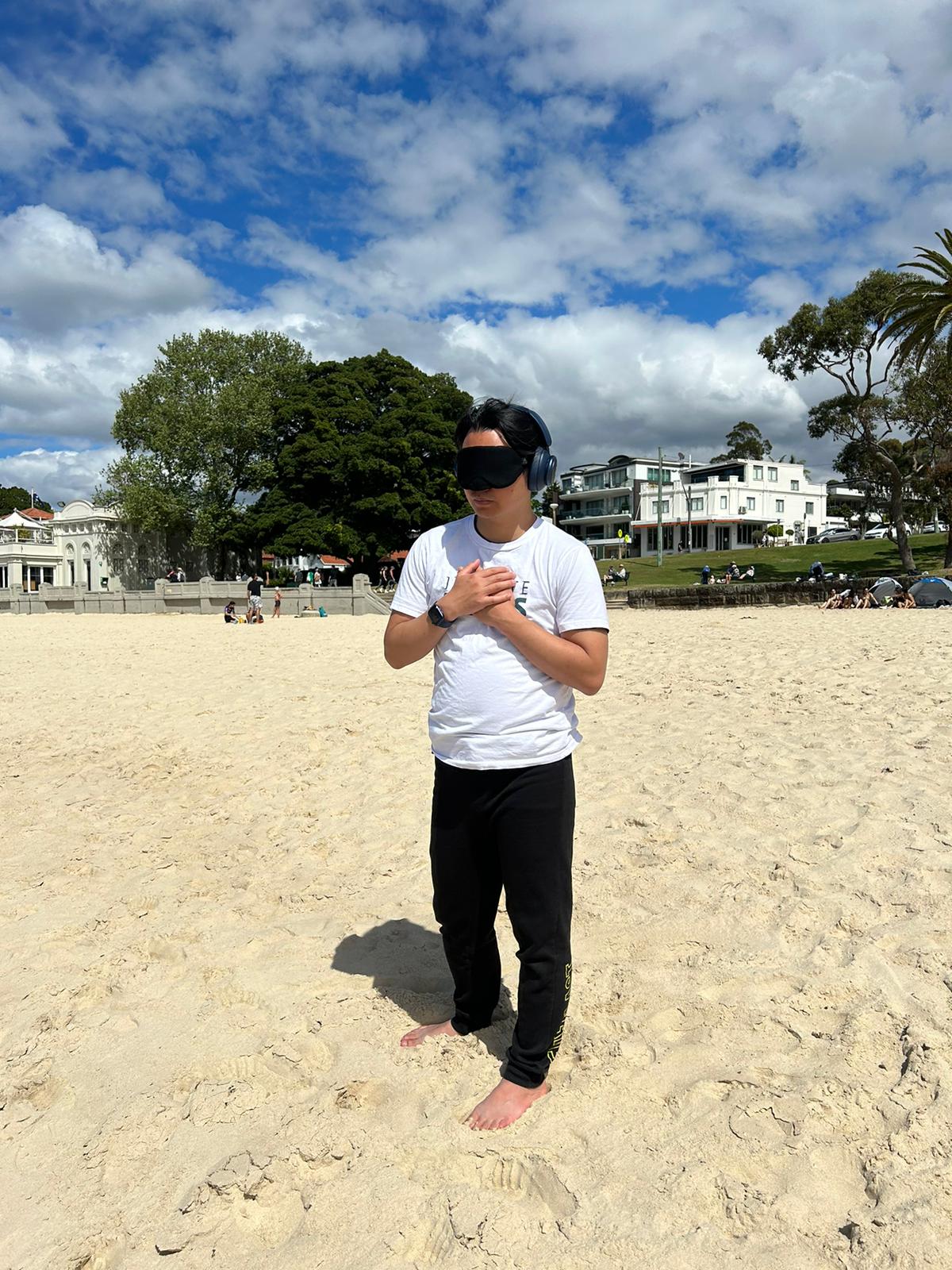 Victor standing with hands on heart at Balmoral Beach, Sydney, the Bathers' Pavilion behind him.